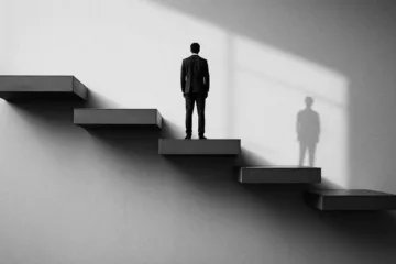 A person in a suit stands on one of several floating steps, facing a wall with light streaming in, casting a shadow a striking representation of consistency amidst uncertainty.