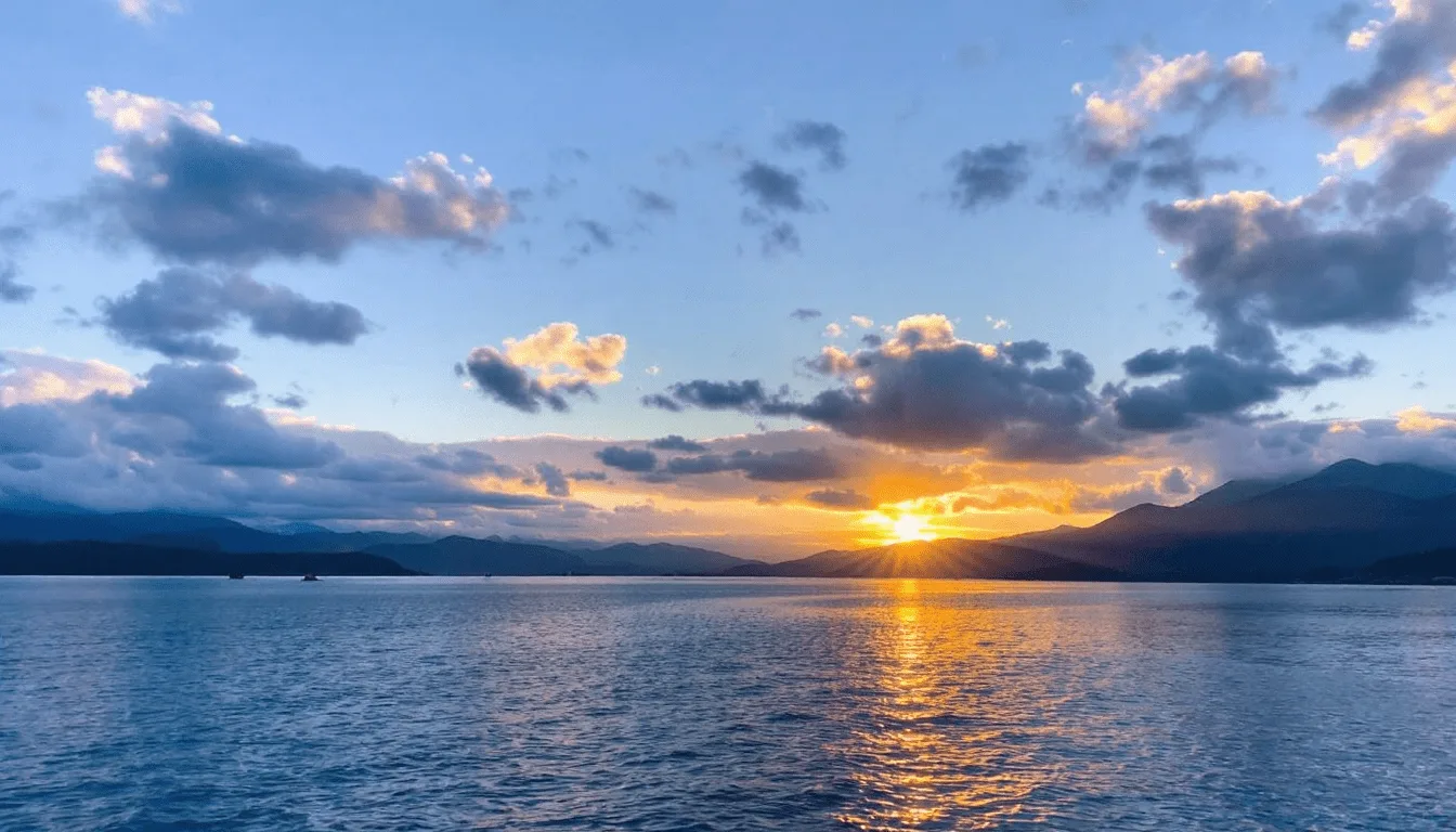 The sun sets behind mountains, casting a golden reflection on a calm blue lake. Scattered clouds dot the sky, creating a serene landscape that inspires faith and nurtures health amidst tranquil beauty. Faith and Health