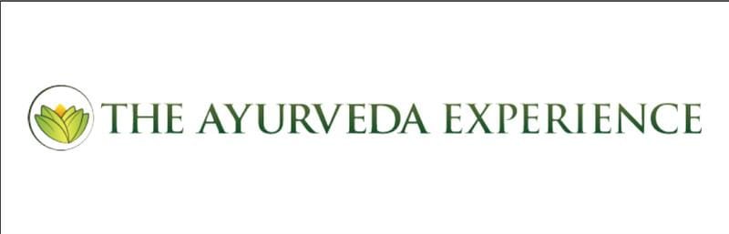 Logo for The Ayurveda Experience features a green stylized lotus inside a circle on the left, followed by "The Ayurveda Experience" in bold green capital letters on a white background.
