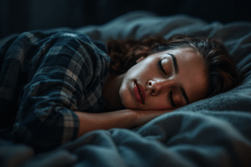 A woman with brown hair wearing a plaid shirt follows her sleep routine, sleeping peacefully on her side in a dimly lit room, resting her head on her hand and lying on a cozy bed with soft bedding.